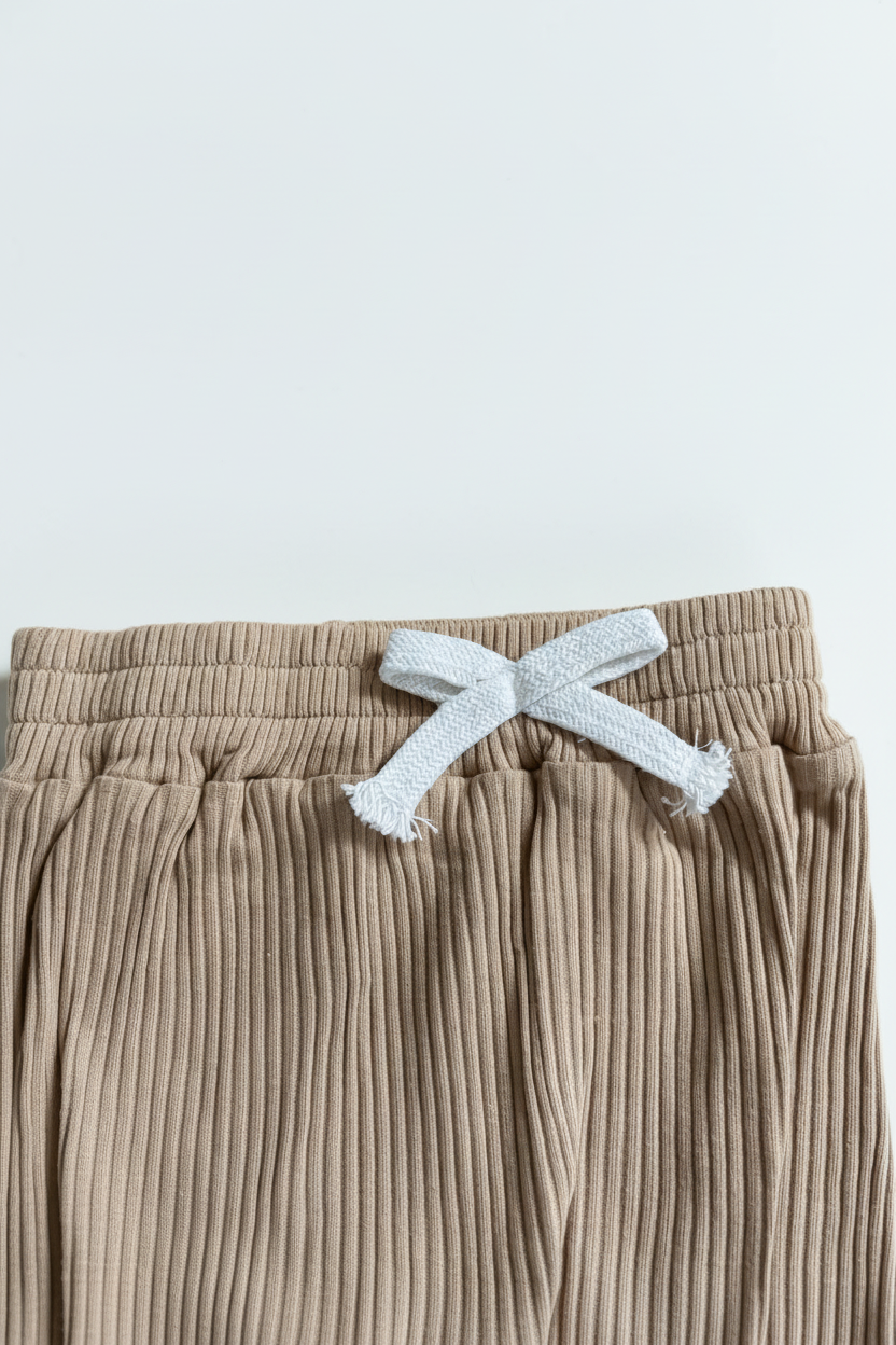 Beige ribbade babybyxor – närbild på midjeband med vit rosett, vit bakgrund